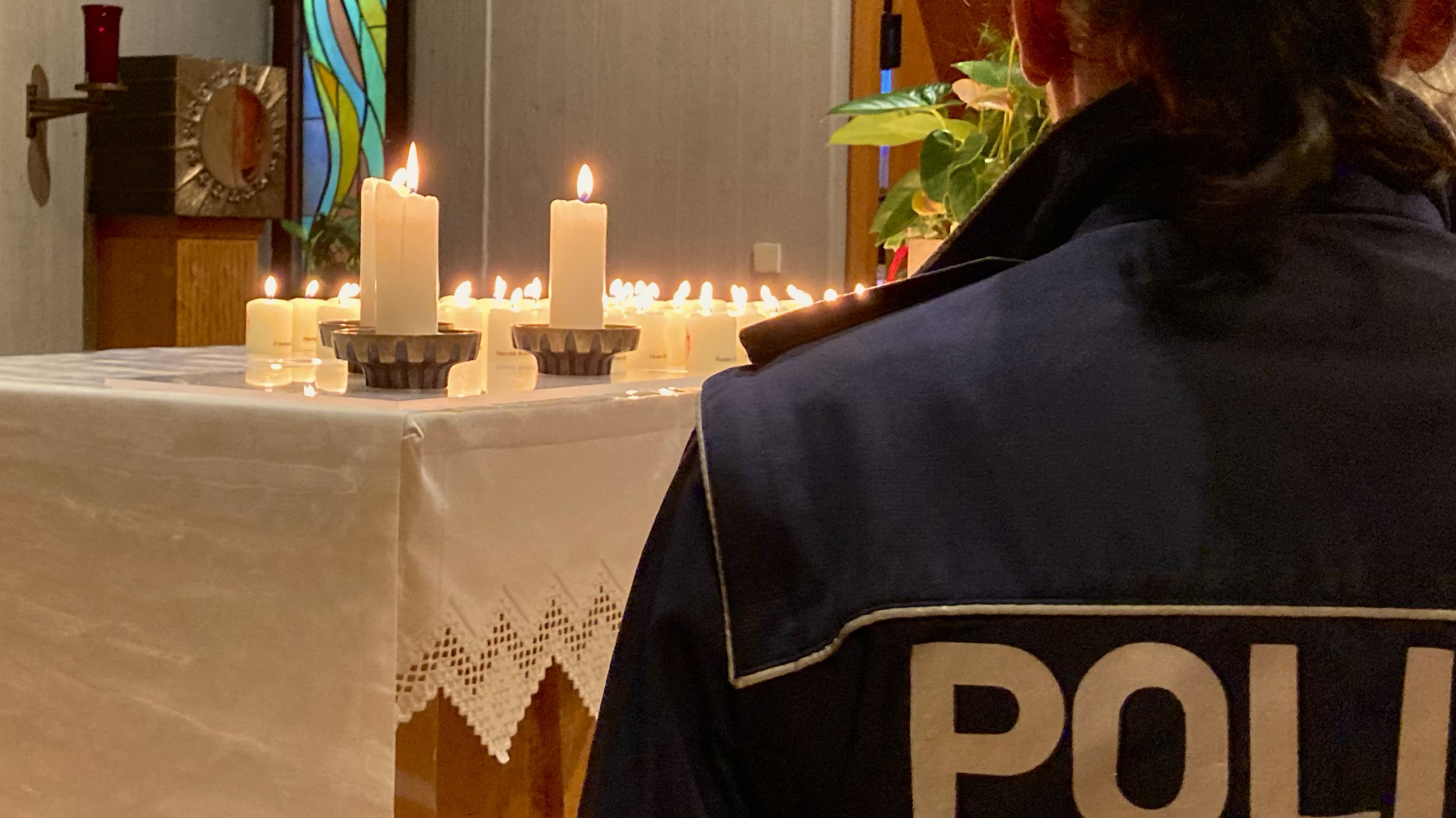 Polizistin steht vor einem Altar mit brennenden Kerzen.